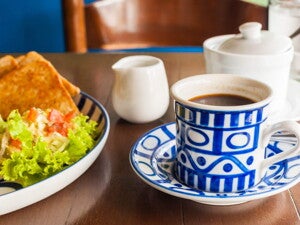 Una taza blanca y azul que contiene café y al lado un plato con ensalada verde y quesadillas