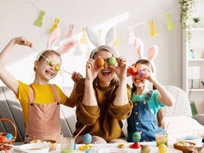 Padres y niños celebrando Pascua, cubriendo sus ojos con huevos de colores de forma divertida.