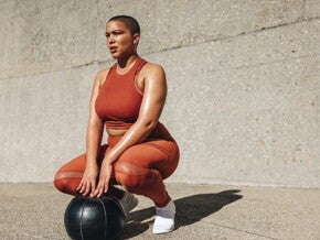Mujer en ropa deportiva realizando ejercicios de Kegel al aire libre con pelota de fitness.