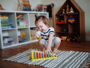 Niña de dos años jugando sobre la alfombra con ábaco de madera. Juego tranquilo como rutina diaria.