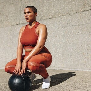 Mujer en ropa deportiva realizando ejercicios de Kegel al aire libre con pelota de fitness.