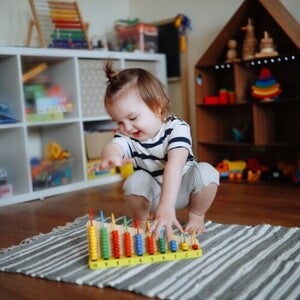 Niña de dos años jugando sobre la alfombra con ábaco de madera. Juego tranquilo como rutina diaria.