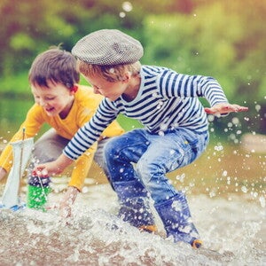 Dos niños pequeños juegan juntos en el agua, lanzando y persiguiendo un barco de juguete, mostrando interacción social en un entorno natural.