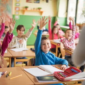 Niños participando en clase y levantando la mano mientras desarrollan hábitos de estudio en un aula escolar.