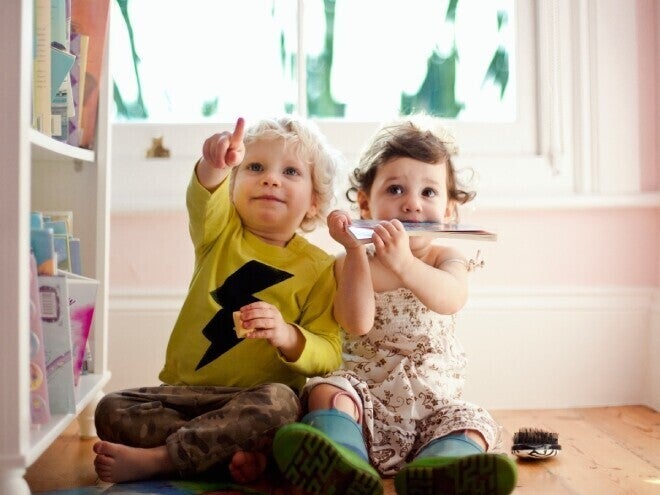 Niño y niña de dos años sentados en el piso, señalando. Concepto de comunicación y desarrollo de lenguaje.