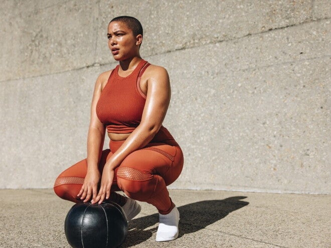 Mujer en ropa deportiva realizando ejercicios de Kegel al aire libre con pelota de fitness.