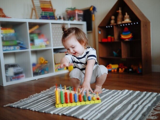 Niña de dos años jugando sobre la alfombra con ábaco de madera. Juego tranquilo como rutina diaria.