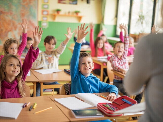 Niños participando en clase y levantando la mano mientras desarrollan hábitos de estudio en un aula escolar.