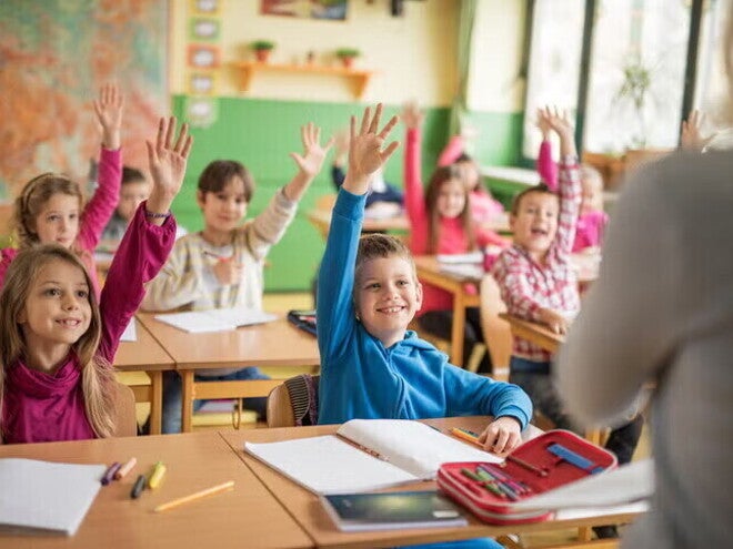 Niños participando en clase y levantando la mano mientras desarrollan hábitos de estudio en un aula escolar.