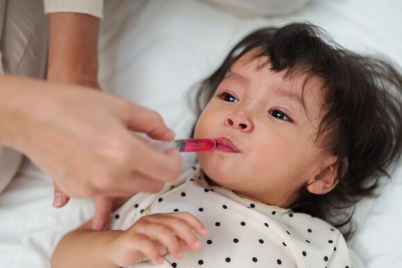 Persona adulta administrando medicamento líquido a un niño pequeño con una jeringa dosificadora.