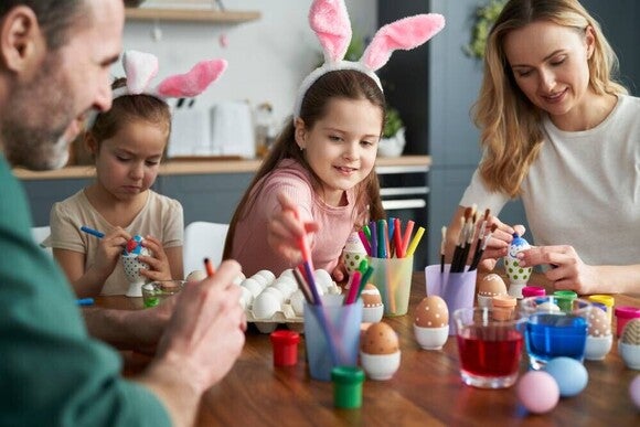 Familia caucásica feliz de cuatro personas decorando huevos de Pascua en casa.