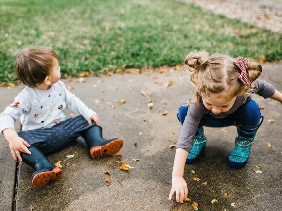 Niño y niña de dos años jugando afuera con hojas de la vereda, actividad para estimular el lenguaje