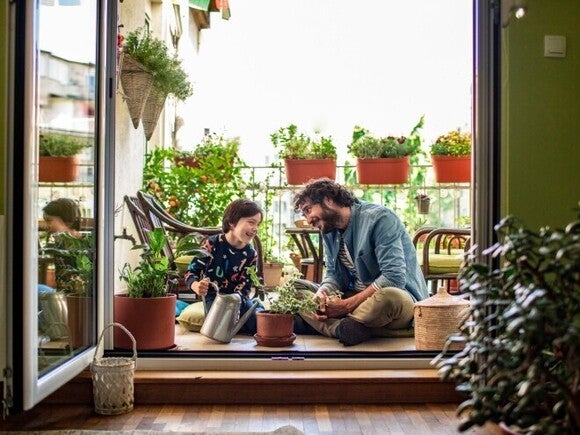 Padre e hijo sonriendo, sentados en el piso, regando plantas con una regadora.