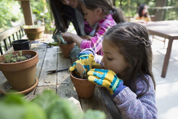 Niña con guantes de jardinería plantando en una maceta mientras comparte la actividad con otros niños, ejemplo de interacción social educativa.
