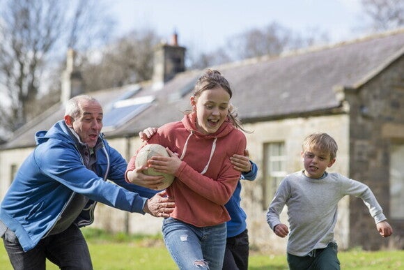 Grupo de niños y un adulto jugando en el jardín de una casa, demostrando interacción social y trabajo en equipo.