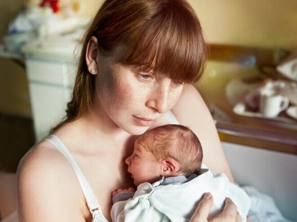 Mamá con posibles señales de depresión posparto sostiene a su recién nacido con expresión de tristeza